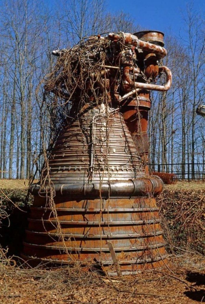 picture of a museum piece Saturn 5 rocket engine, covered in natural overgrowth probably during the pandemic